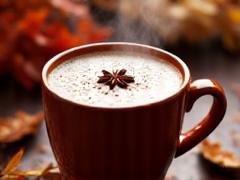 Steaming mug of chai latte with autumn leaves as garnish.
