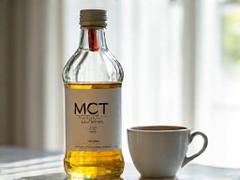 Clear bottle of MCT oil next to a coffee cup.